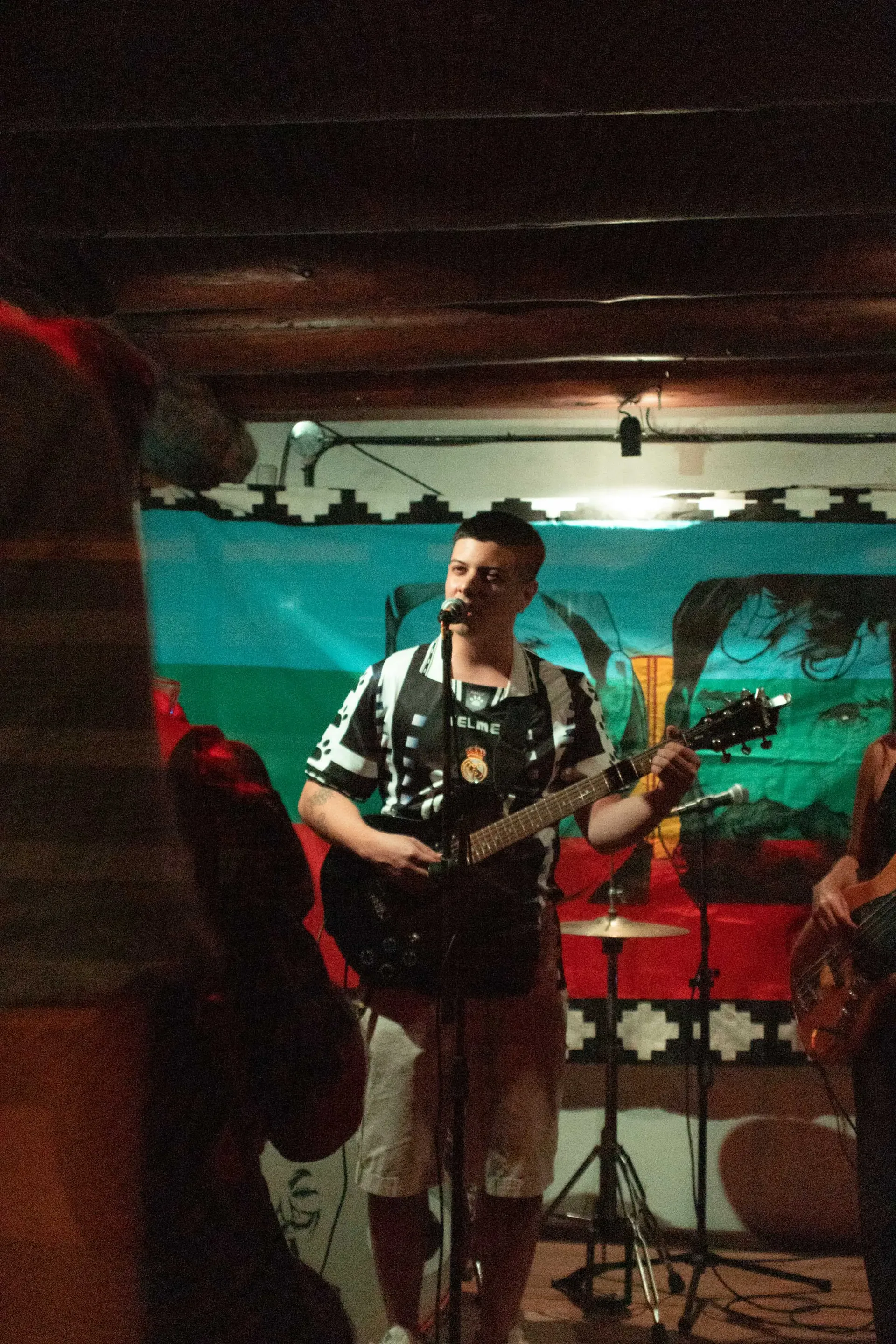 Guitarrista cantando en vivo en un salón con un mural de fondo