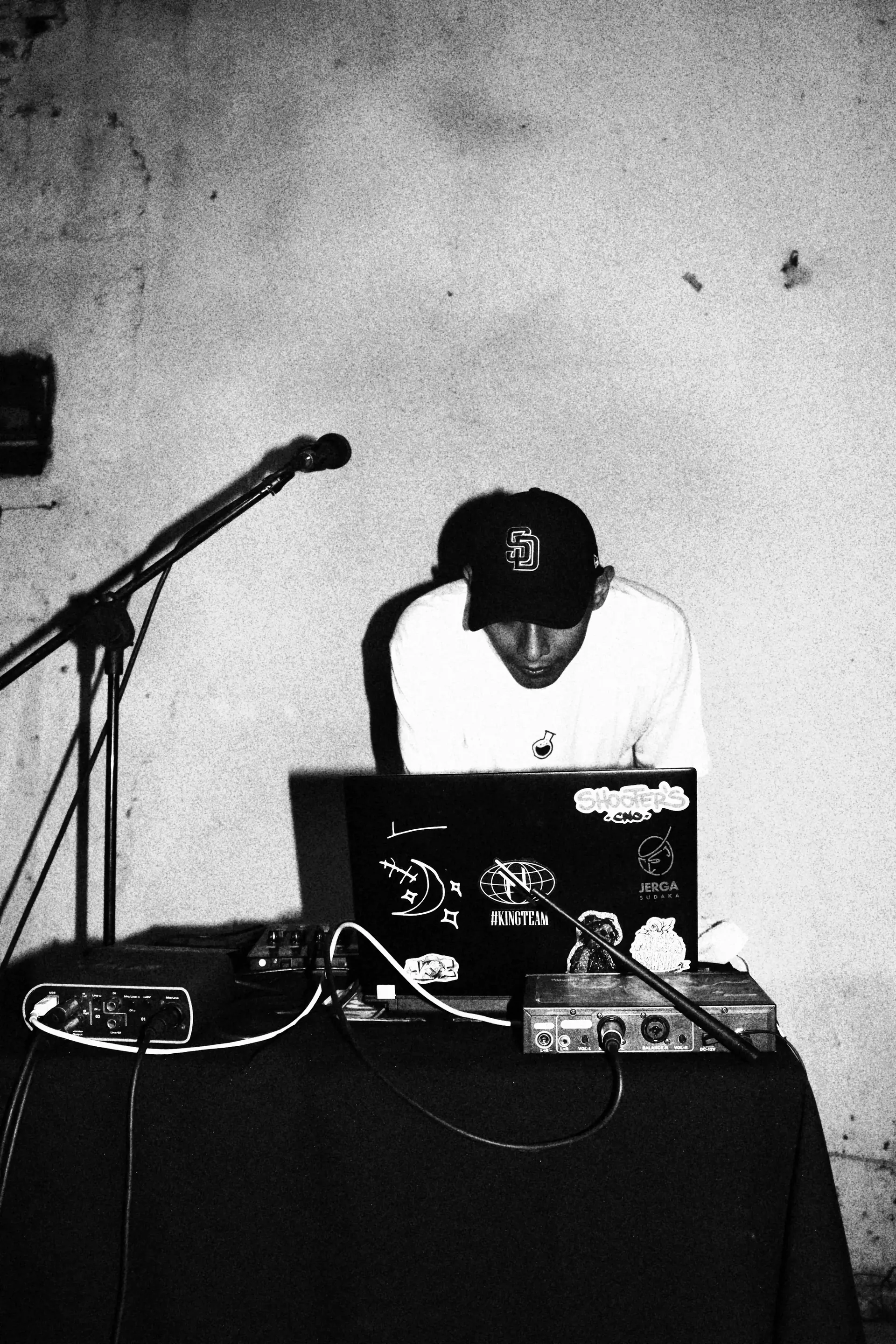 Productor musical con gorra frente a su controladora en una pared descascarada, blanco y negro