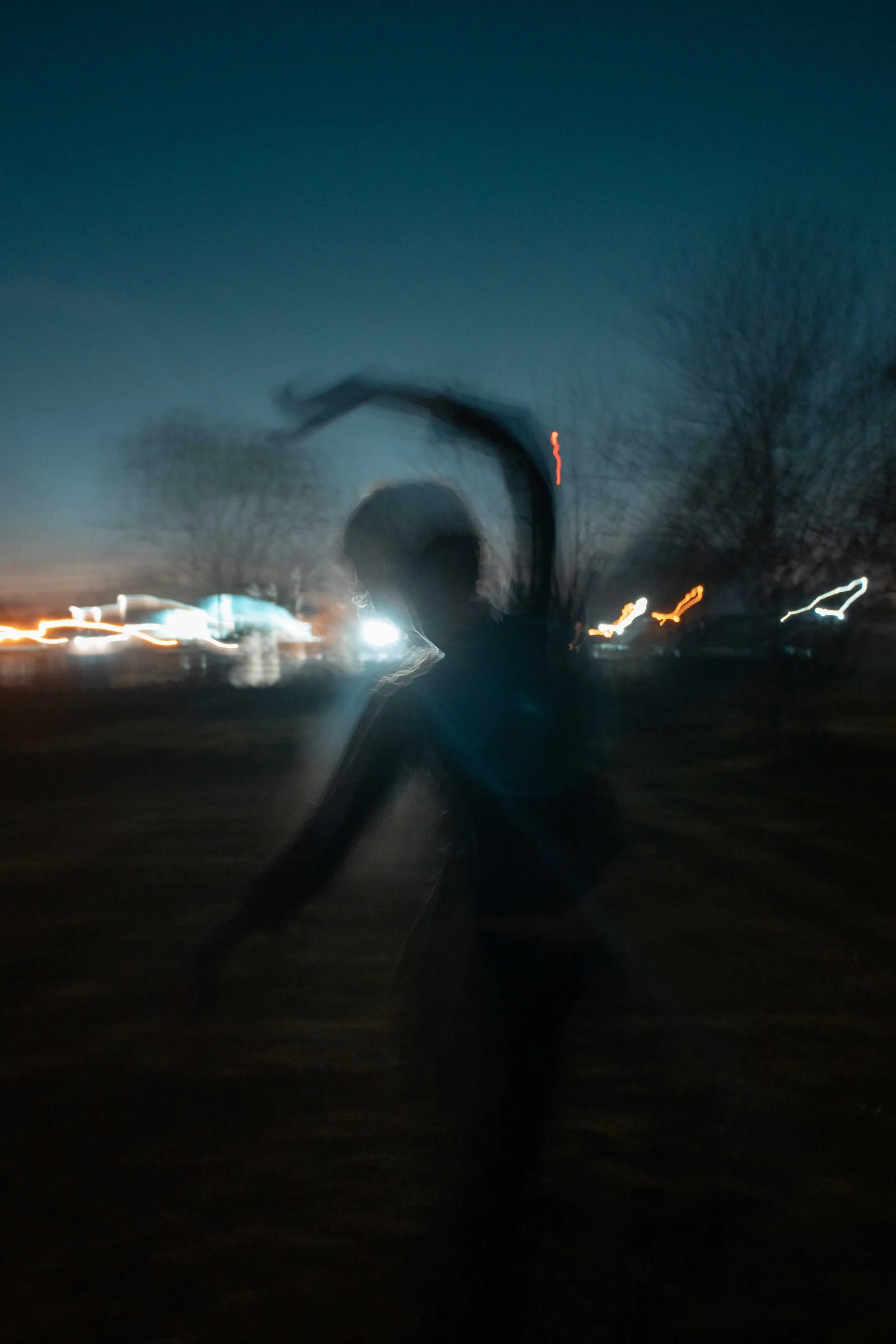 Silueta bailando en el campo al anochecer con luces de fondo
