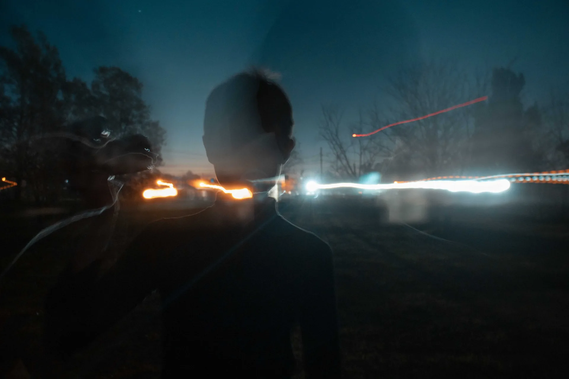Dos siluetas de noche junto a la ruta entre estelas de luces de autos